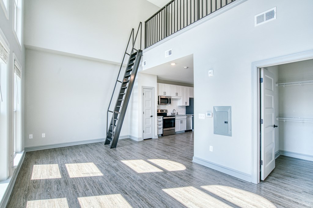 an empty living room with a staircase and a kitchen