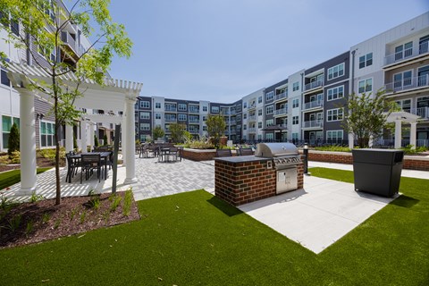 A patio area with a table and chairs is surrounded by a grassy area and apartment buildings.