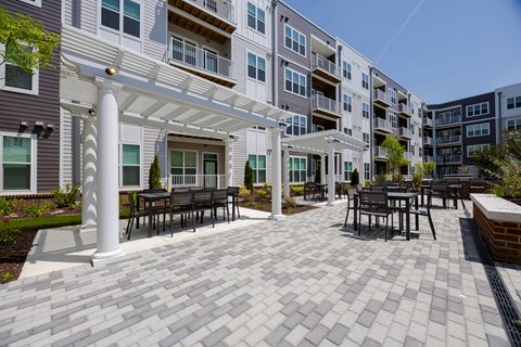 A patio with a white pergola and black chairs.