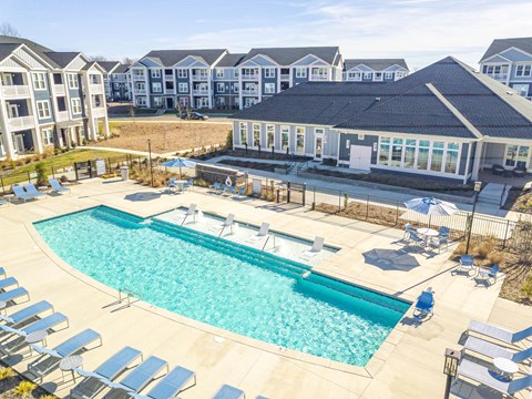 A large swimming pool surrounded by sun loungers and umbrellas in front of apartment buildings.