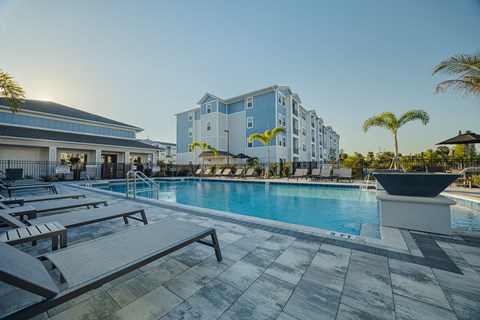 A pool area with sun loungers and a building in the background.