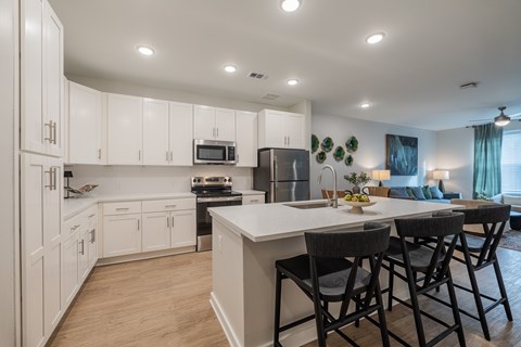 A kitchen with white cabinets and a large island with four chairs.