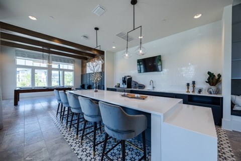 A modern kitchen with a long white island and blue chairs.