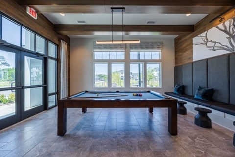 A pool table is in the middle of a room with a bench and a window.