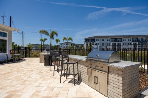 A patio with a grill and chairs is set up on a tiled floor.