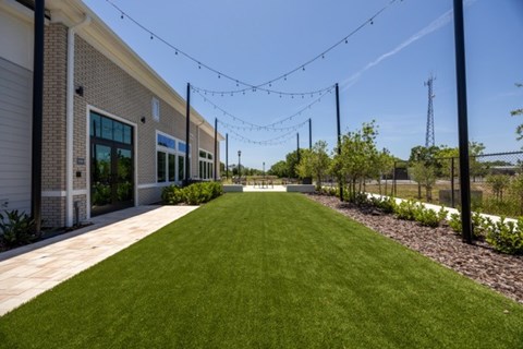 A long grassy area in front of a building with lights strung above it.