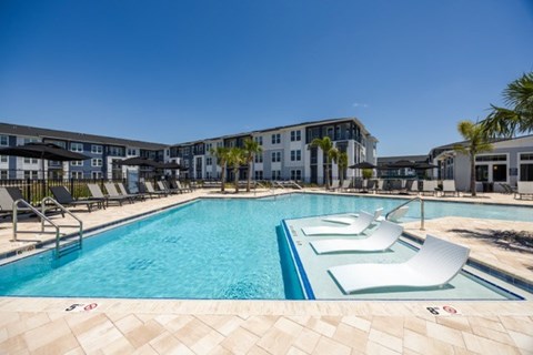 A large swimming pool with lounge chairs and a building in the background.