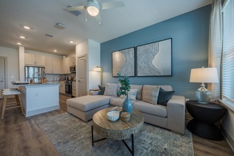 A modern living room with a grey sofa, a coffee table, and a kitchen area in the background.