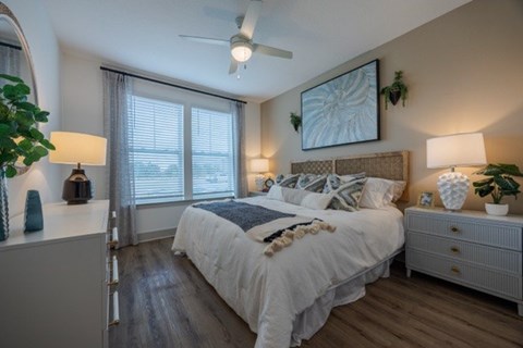 A bedroom with a large bed, a ceiling fan, and a painting on the wall.