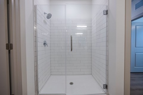 A white tiled shower with a glass door and a white floor.