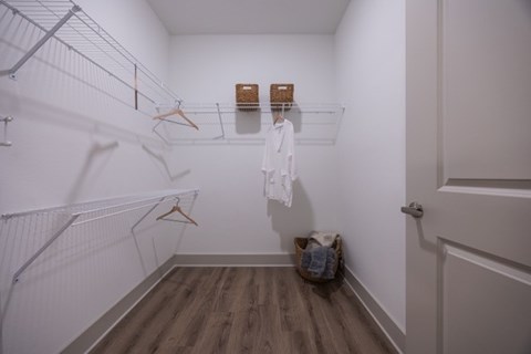 A white closet with clothes hanging and a basket on the floor.