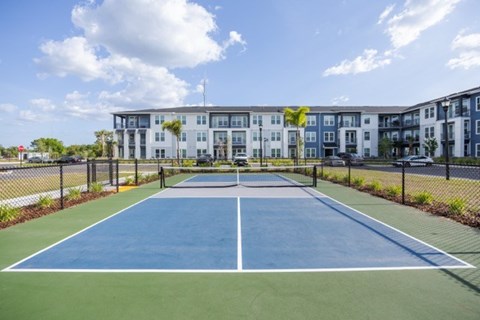 A tennis court is surrounded by a fence and apartment buildings.