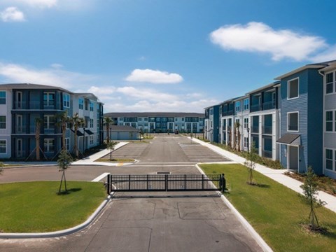 A gated entrance leads to a parking lot in front of a row of townhouses.