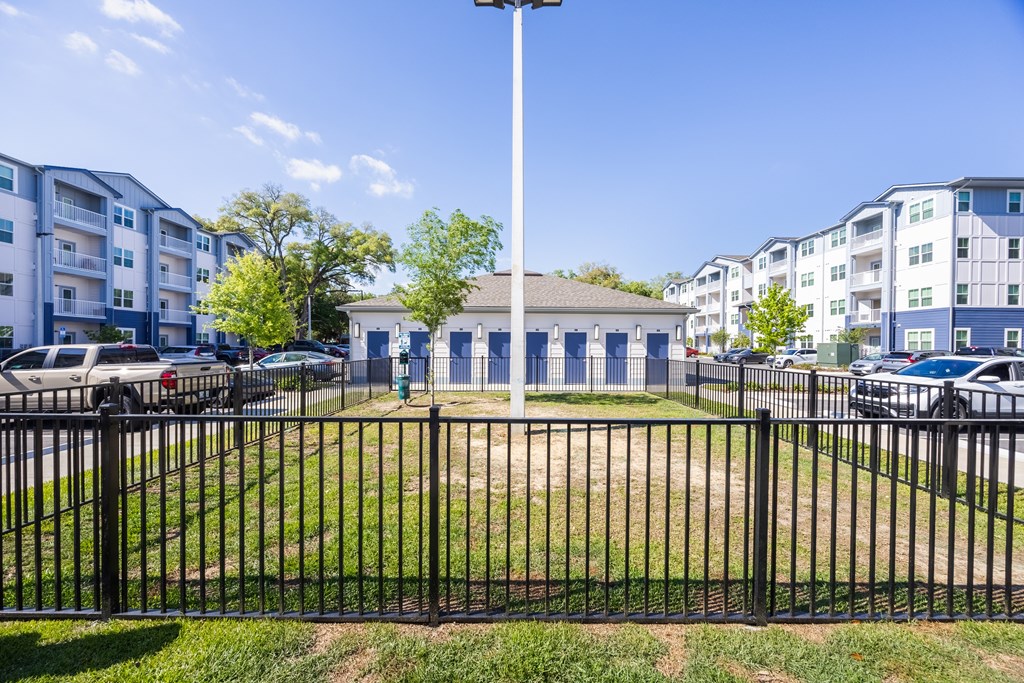 A black fence surrounds a grassy area in front of apartment buildings.