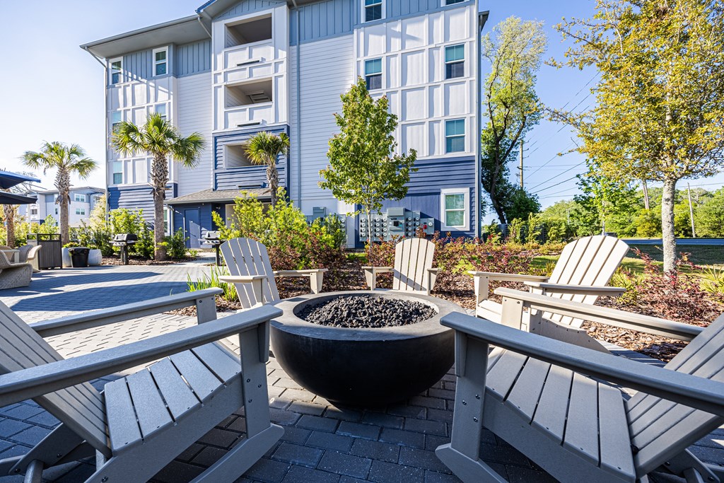 A modern building with a blue and white exterior is surrounded by trees and outdoor furniture.