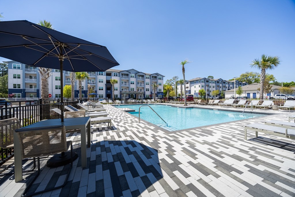A pool area with a black umbrella and a bench.