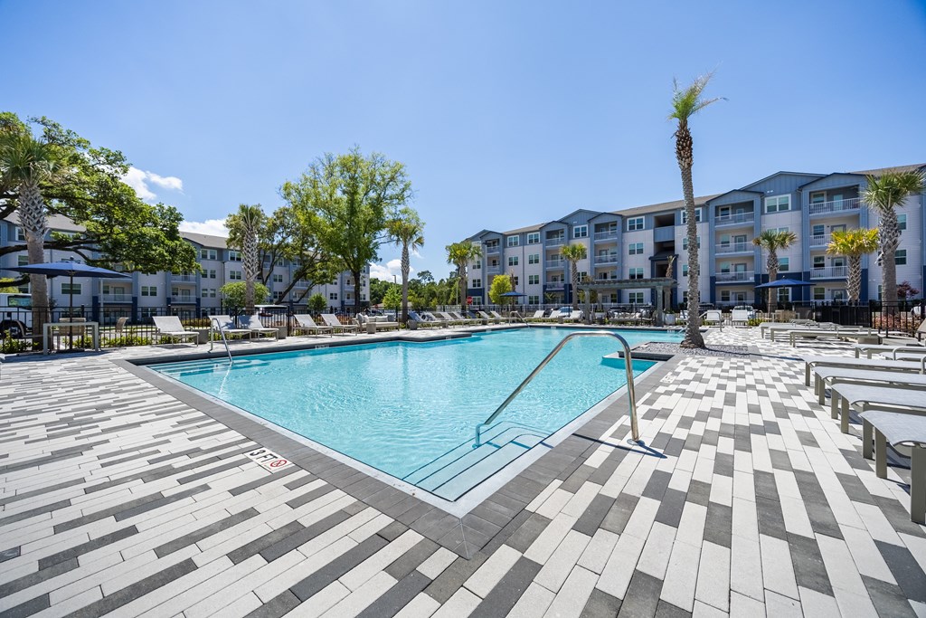 A large swimming pool surrounded by a tiled floor and apartment buildings.