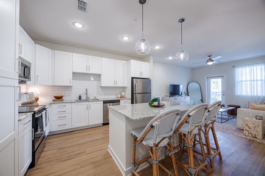 A kitchen with white cabinets and a large island with chairs around it.
