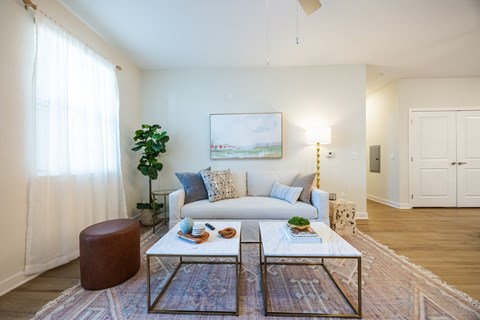 A living room with a white couch, a glass coffee table, and a painting on the wall.
