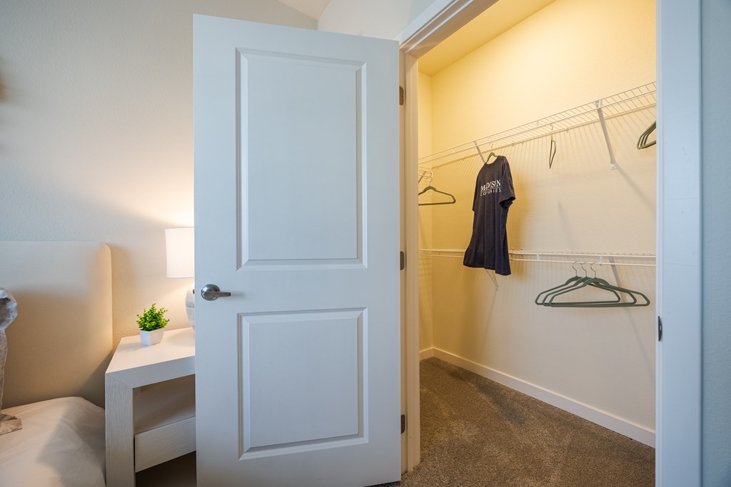 A white door is open to a hallway with a black shirt hanging on a hanger.
