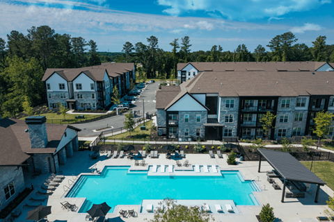 A large swimming pool surrounded by lounge chairs and umbrellas in front of apartment buildings.