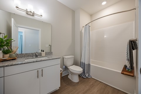 A white toilet sits in a bathroom with a grey shower curtain.