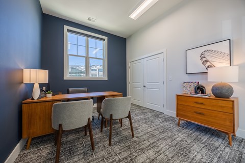 A room with a desk, chairs, and a framed picture on the wall.