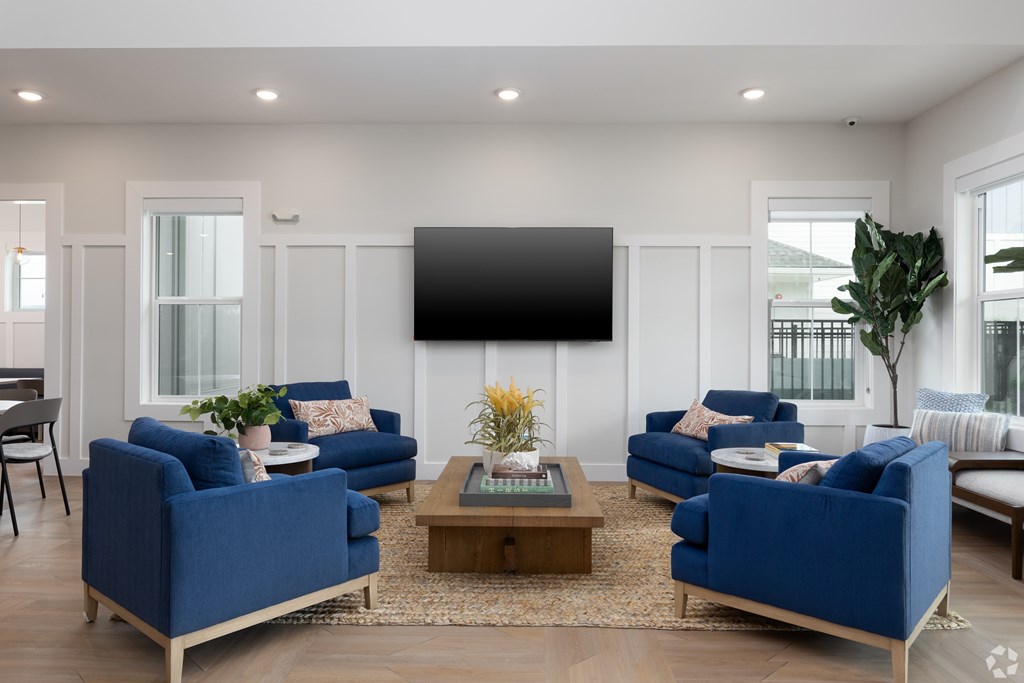 A living room with blue sofas and a flat screen TV mounted on the wall.