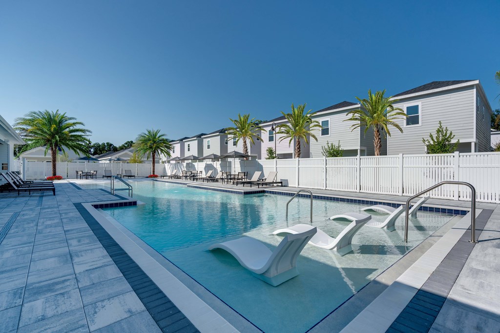 A pool with a white fence and palm trees in the background.