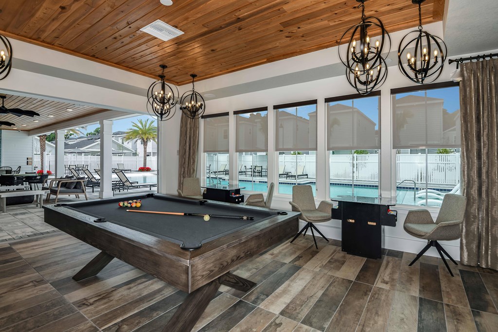 A pool table is in the middle of a room with a wood floor and a wooden ceiling.