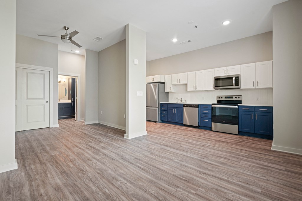 an empty living room and kitchen with white and blue cabinets and wood floors