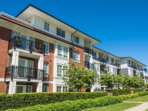 A row of apartment buildings with balconies and green hedges in front.