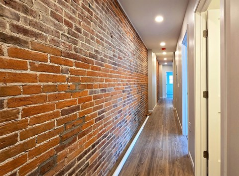 A long hallway with a brick wall on the left and wooden floors.