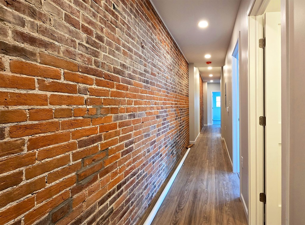A long hallway with a brick wall on the left and wooden floors.