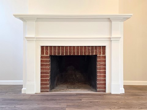 A white fireplace with a brick interior and a wooden mantle.