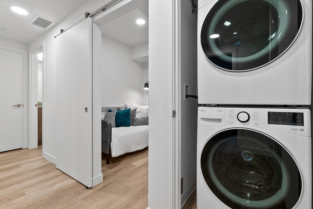 a washer and dryer in a laundry room with a bed in the background