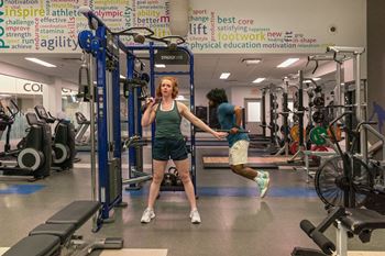 a woman standing in a gym with weights and a man running