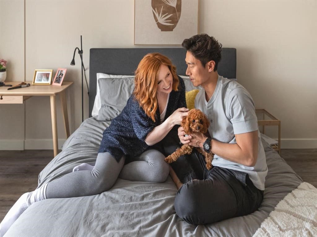 a man and woman sitting on a bed holding a dog