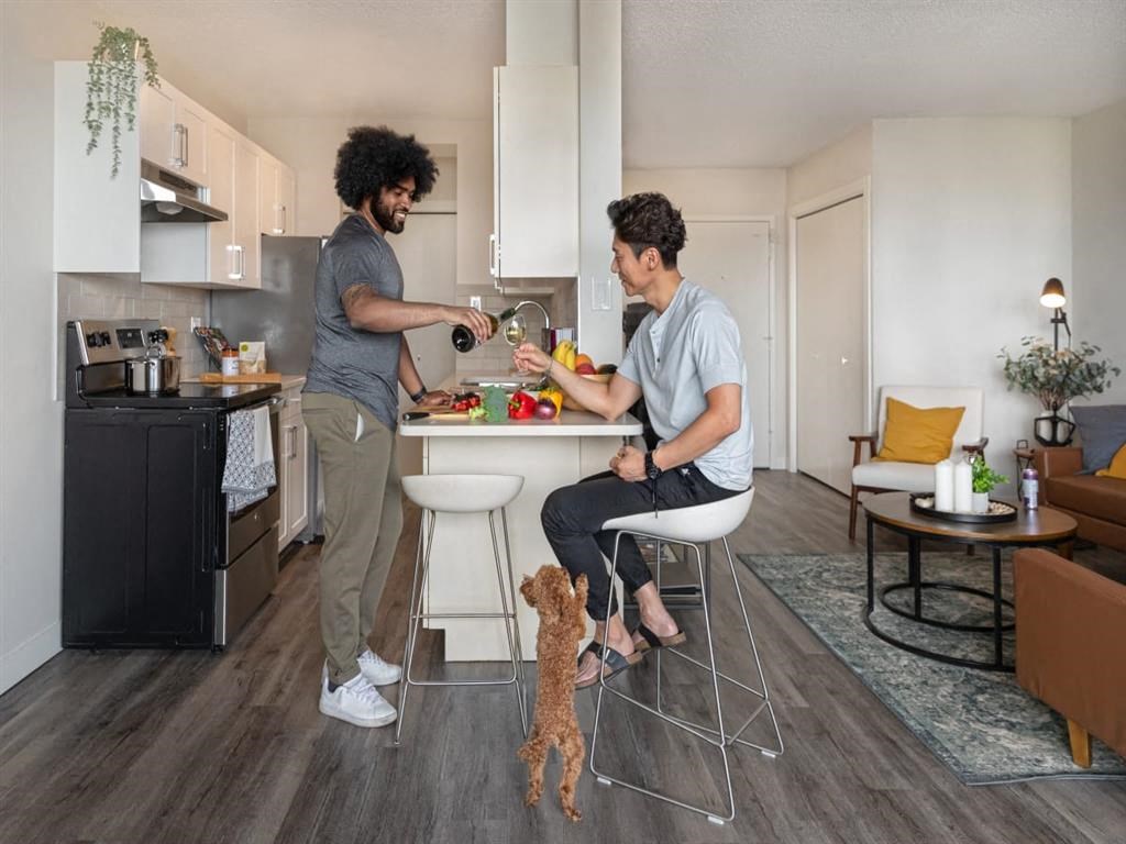 two men in a kitchen with a dog