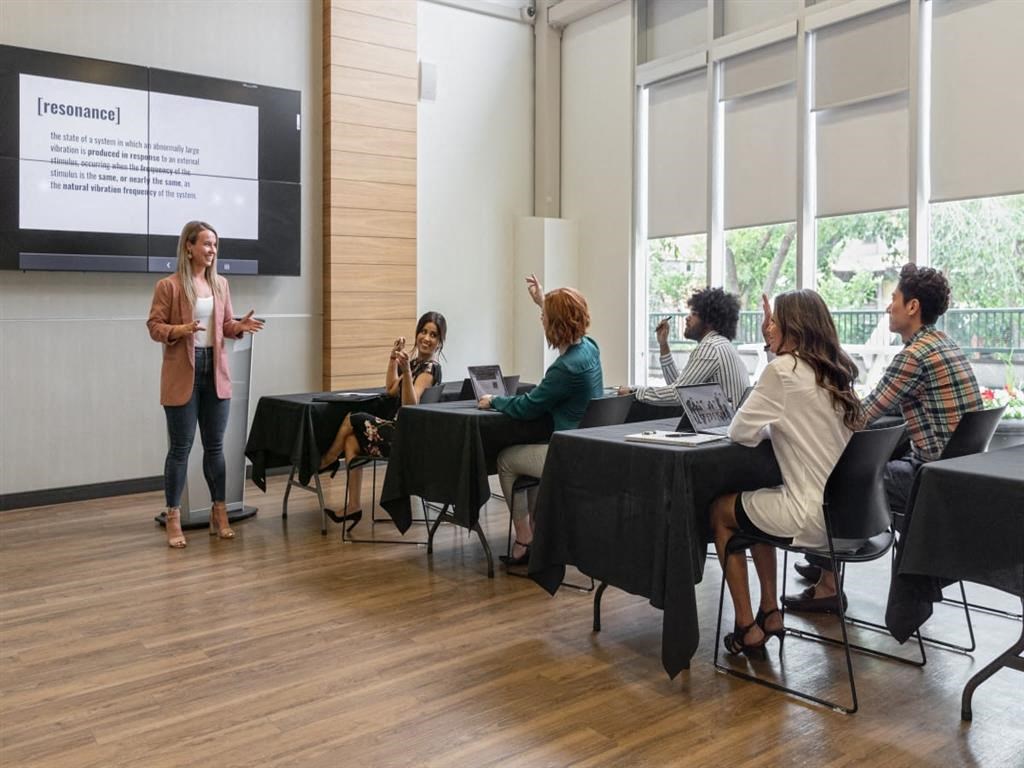 a group of people sitting at tables in a room with a presentation on a screen
