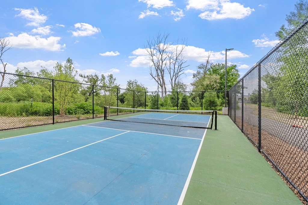 A tennis court surrounded by a fence and trees.