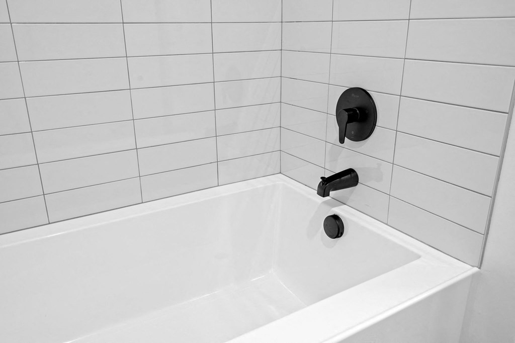 a white tub with a black faucet in a white tiled bathroom