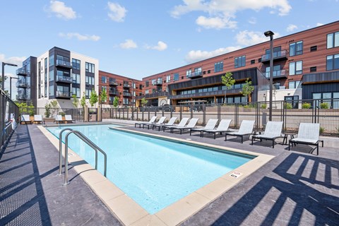 A swimming pool surrounded by lounge chairs and apartment buildings.