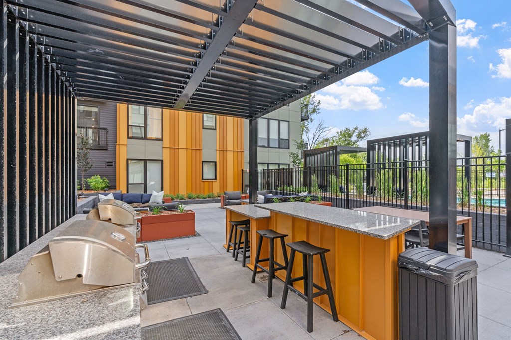 A patio with a bar and stools under a roof.