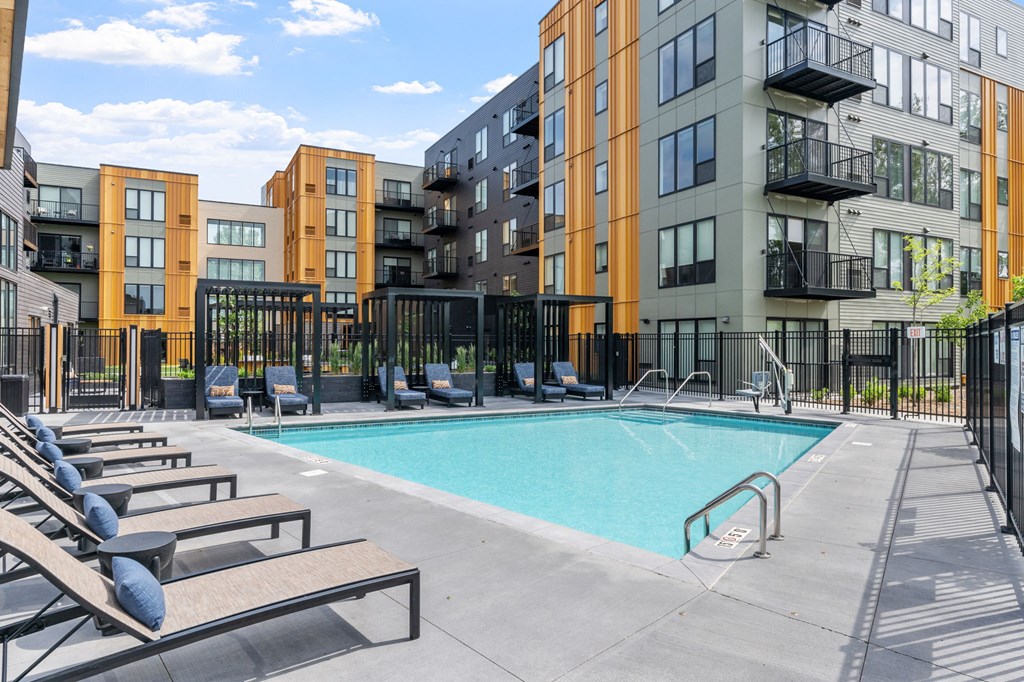 A swimming pool surrounded by lounge chairs and apartment buildings.