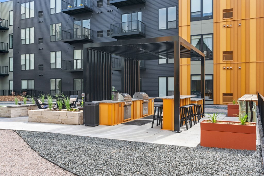 A modern building with a black and orange exterior and a gravel patio area with a bar.