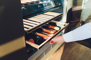 a man is grabbing a bottle of wine from an open refrigerator