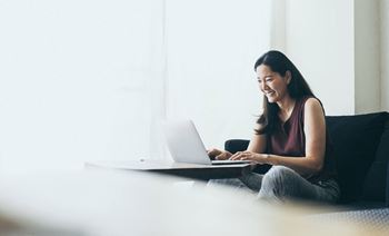 a woman sitting on a couch laughing while using a laptop computer