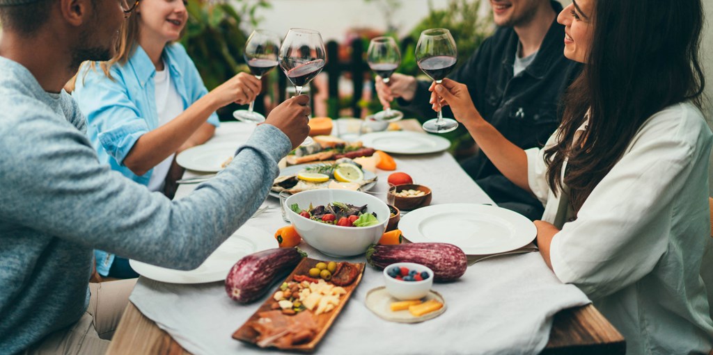 a group of people sitting around a table eating and drinking wine