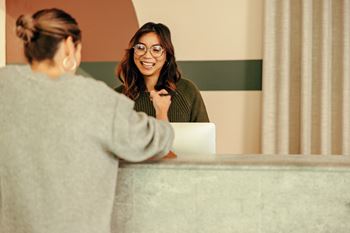 two women talking at a hotel desk with a laptop